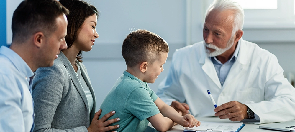 Happy kid and his parents sitting at doctor's office and communicating with senior pediatrician. Focus is on boy.