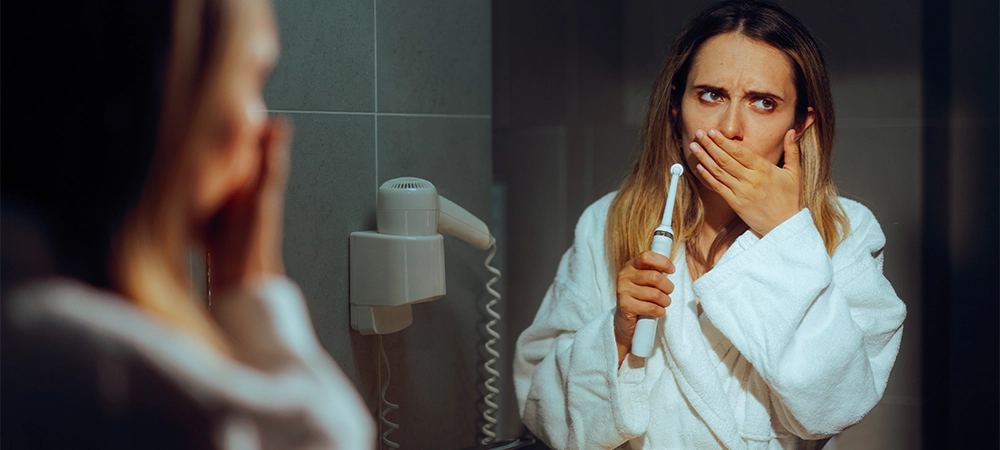 woman feeling pain while brushing her teeth