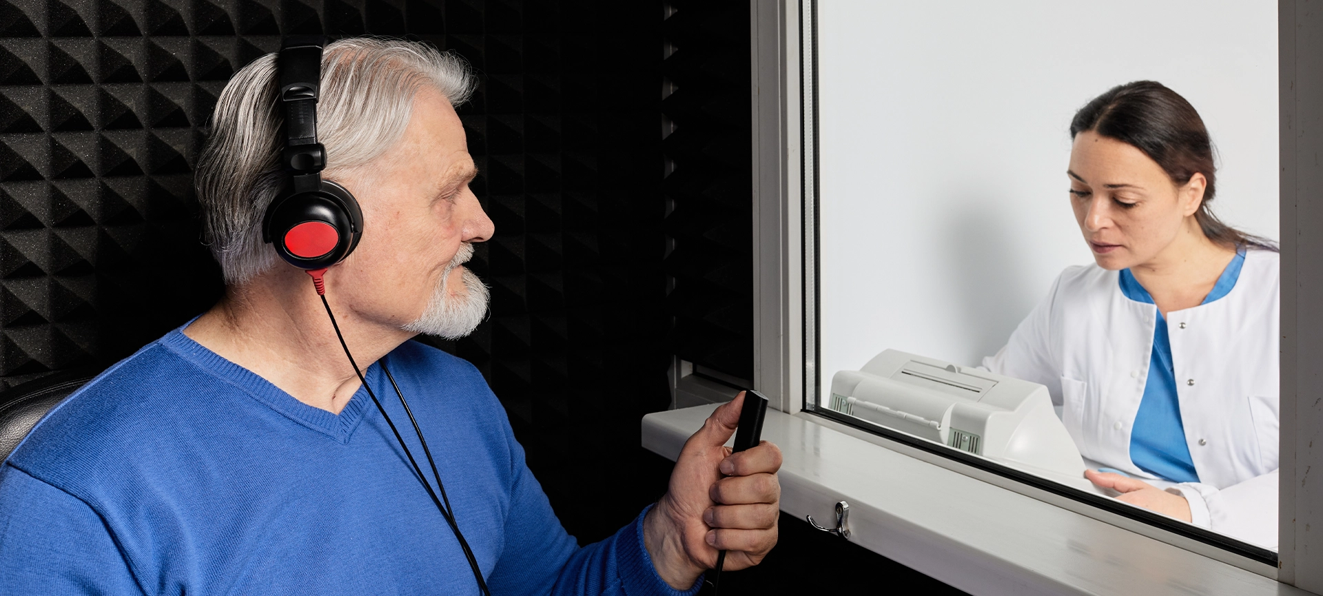 audiologist doing hearing check-up to senior man in soundproof audiometric booth