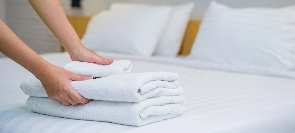 close-up of hands putting stack of fresh white bath towels on the bed sheet