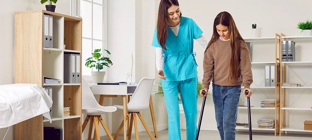 woman doctor helps a little kid child patient girl walk with crutches at the clinic after her leg injury