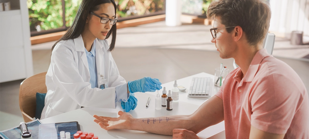 young asian allergist is conducting a prick scratch test to diagnose any allergic reaction on a young male's forearm during a health check visit to a medical clinic