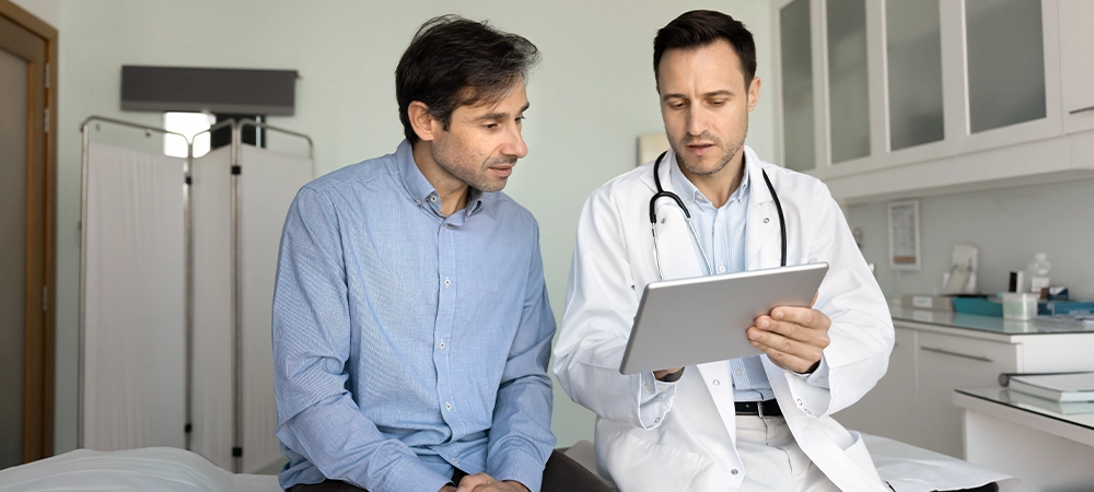 Serious doctor showing electronic checkup results to patient, using tablet computer, talking to man, explaining medical report, diagnosis after examination in clinic office