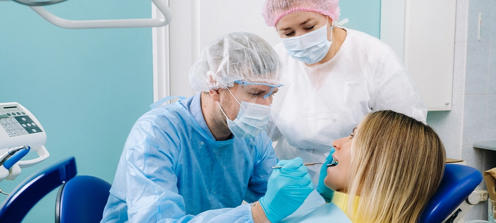 The patient smiles in the dentist's chair in a protective mask and instrument before treatment in the dental office.