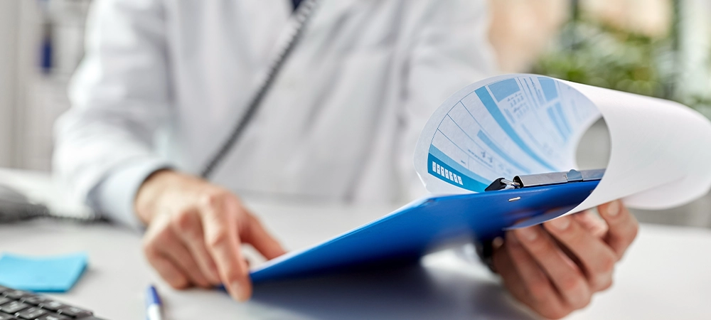 healthcare, medicine and people concept - male doctor with clipboard calling on desk phone at hospital