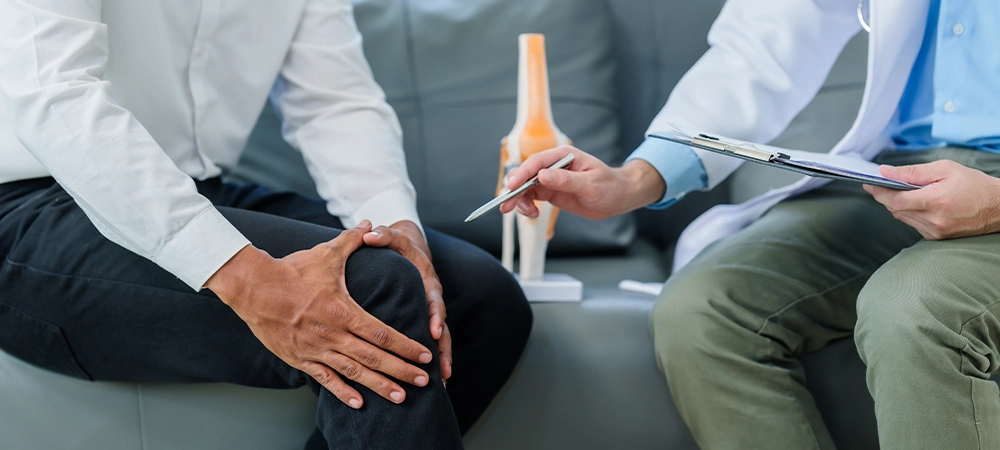 Doctor is seeing a patient. sitting and holding his knees with discomfort Meanwhile, bone model. talking about knee pain or osteoarthritis.