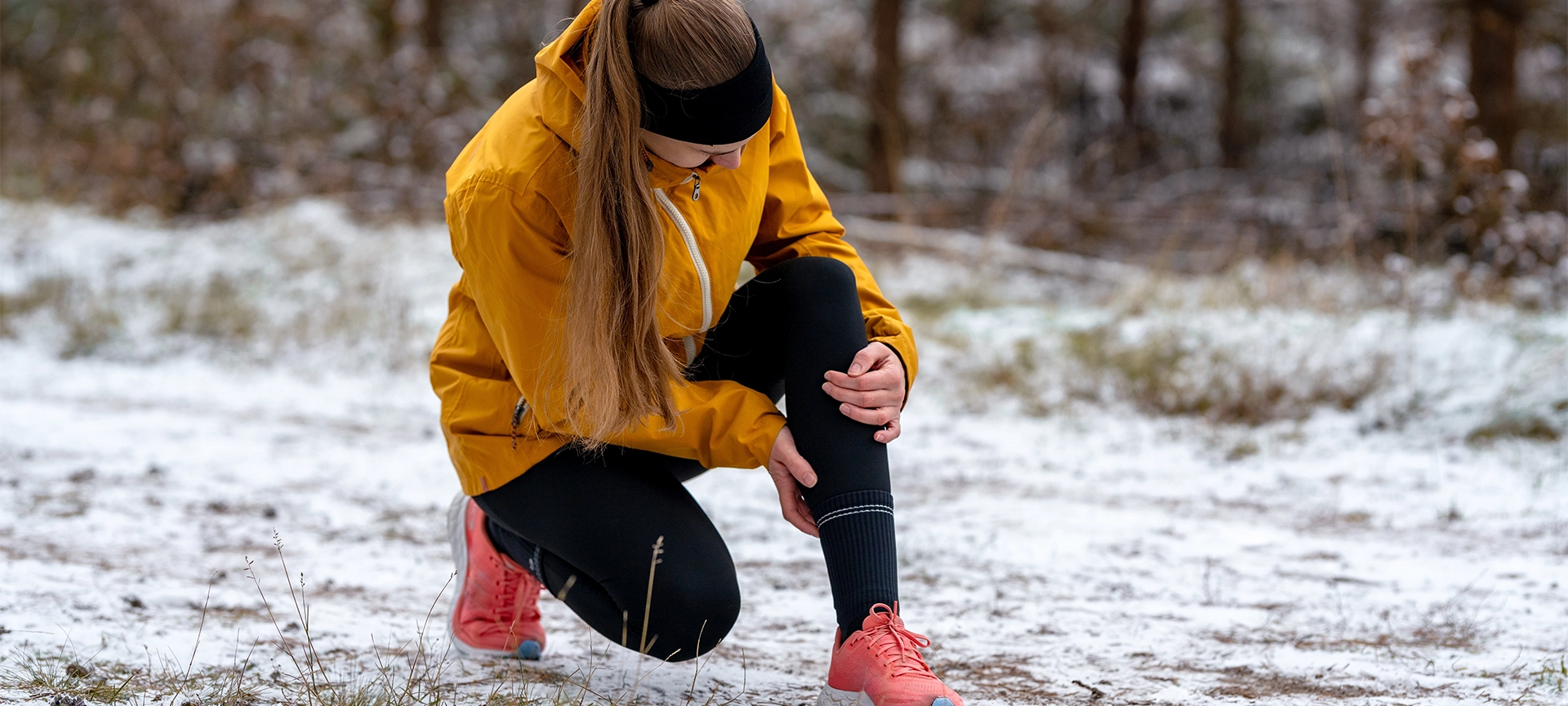 Close-up of a female runner clutching her knee, having stopped on a snowy trail. Sports injury or sudden training setback in cold winter weather.