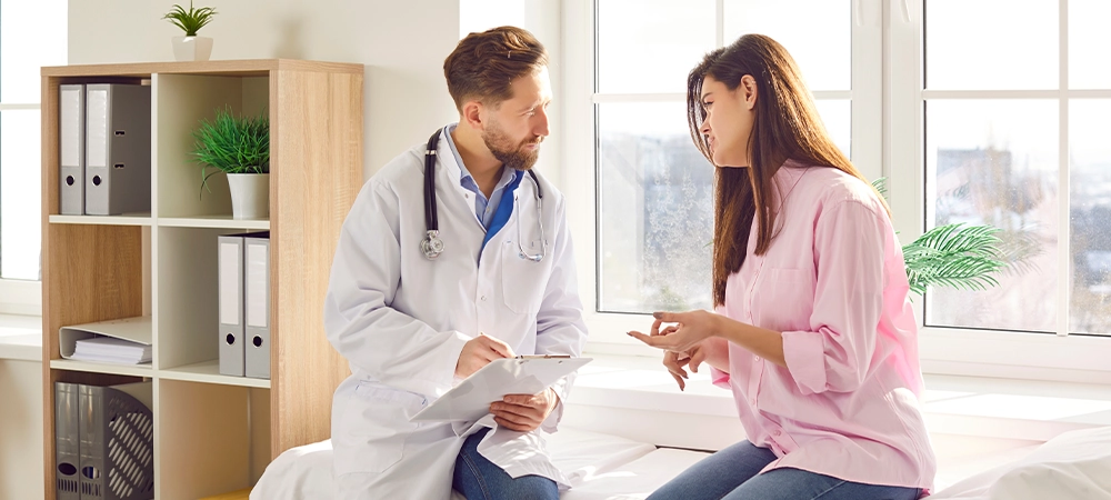 Male doctor, man consulting female patient for treatment, rehabilitation, regular health check up. Physical therapist in medical clinic room listening to woman couch sitting, describing symptoms