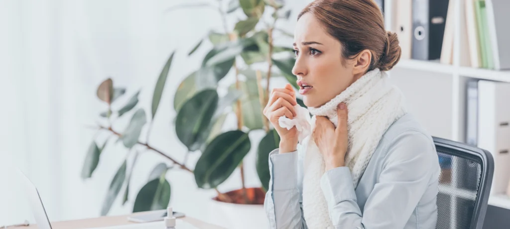 adult sick businesswoman with flu sitting at workplace in scarf