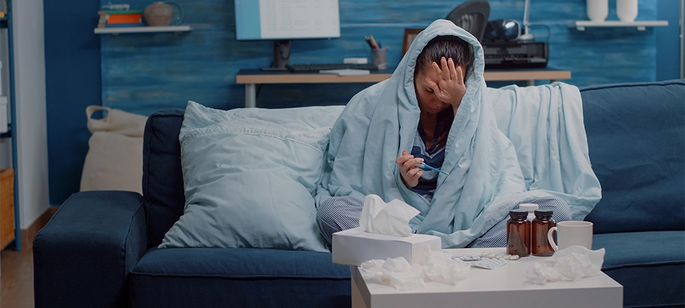 Person wrapped in blanket holding thermometer for fever